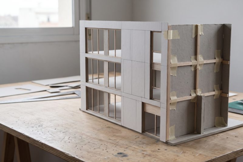 Maqueta de una fachada sobre una mesa de taller, con los soportes y la estructura posterior a la vista.